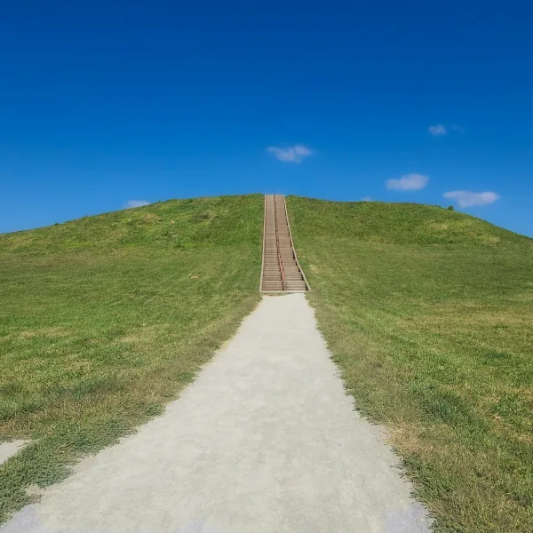 Wide view of the stairway leading up Monk’s Mound at Cahokia, the largest Native American earthwork north of Mexico, with green grass and a vivid blue sky.