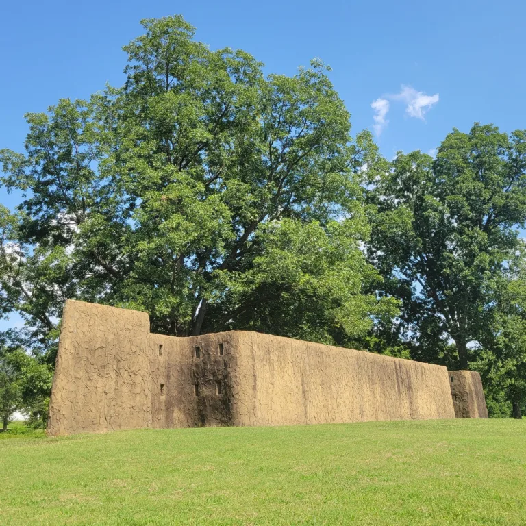Reconstructed section of the timber-and-earth palisade wall at Angel Mounds State Historic Site in Indiana, showing defensive architecture under a clear summer sky.