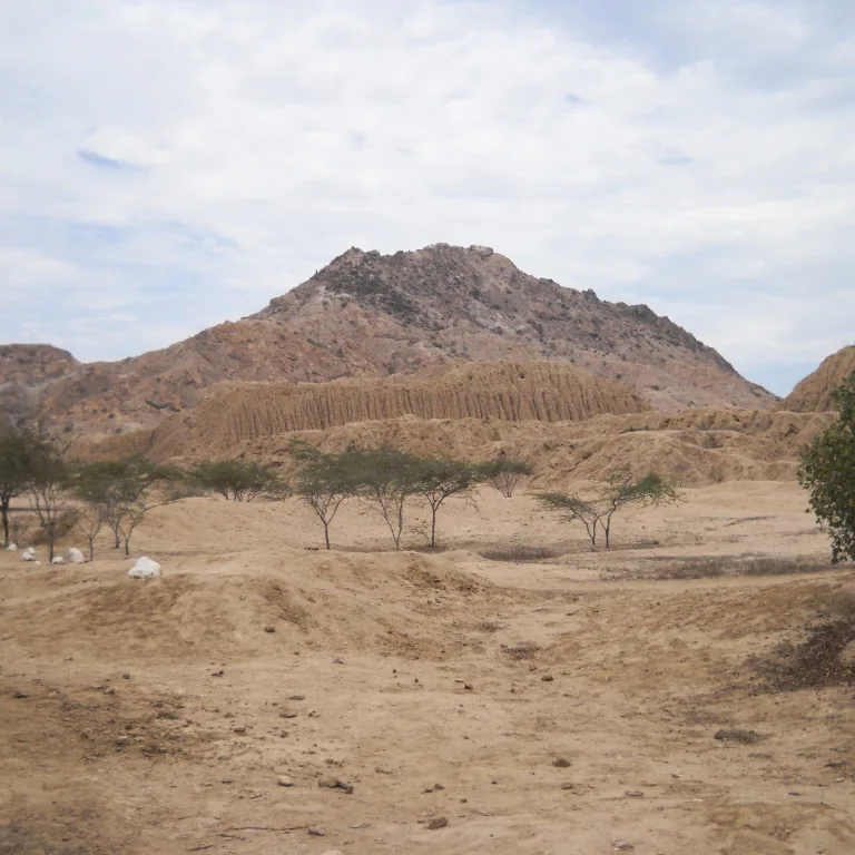 View of an adobe huaca at the Túcume archaeological site, framed by dry desert terrain and a rugged mountain in the background