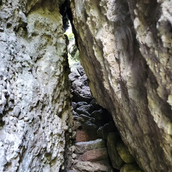 Narrow stone corridor beneath the El Tlatoani ruins, showing natural rock walls and shadowed steps