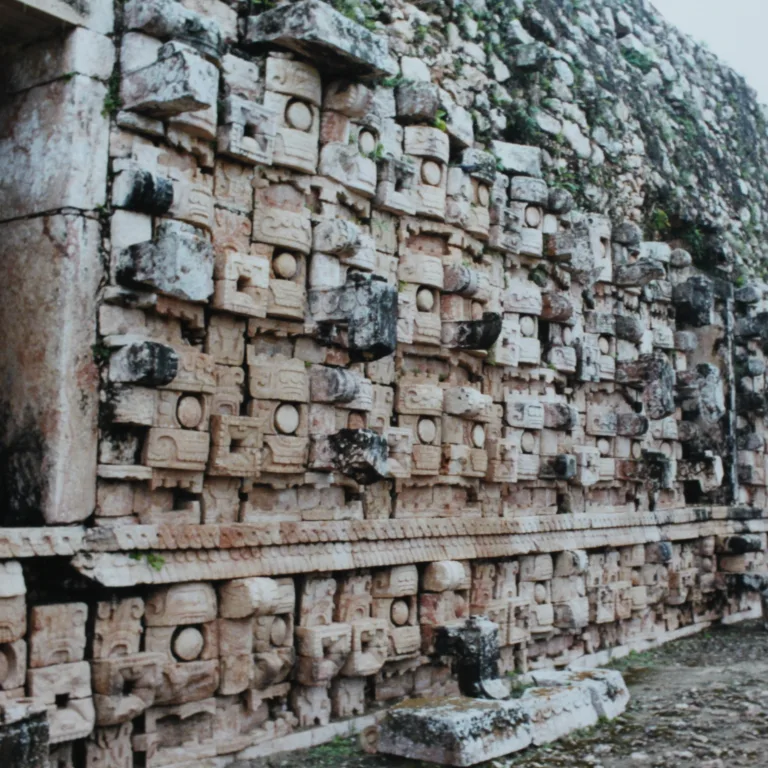 Close-up view of the Palace of the Masks at Kabah, showing rows of carved Chac deity faces in classic Puuc architectural style