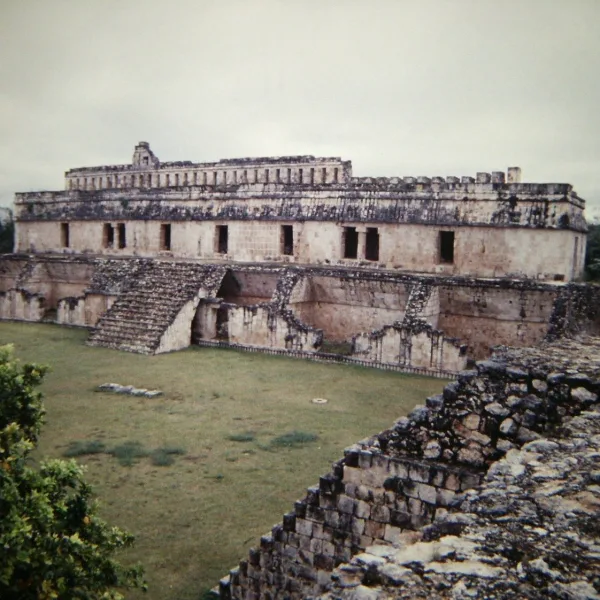 View of the Palace of the Masks at Kabah, a multi-tiered Maya structure with detailed Puuc-style stonework and columns in Yucatán, Mexico.