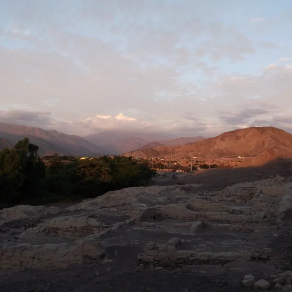 Wide view across the Nazca basin from Los Paredones with orange-pink light hitting the distant Andes mountains