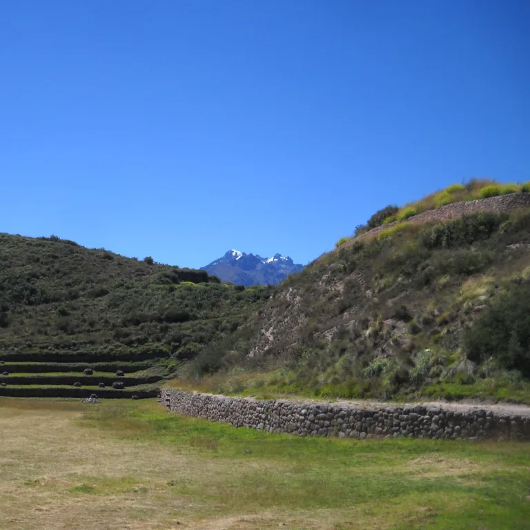 Distant snow-capped Andes mountains visible beyond grassy Inca terraces at Moray archaeological site in Peru