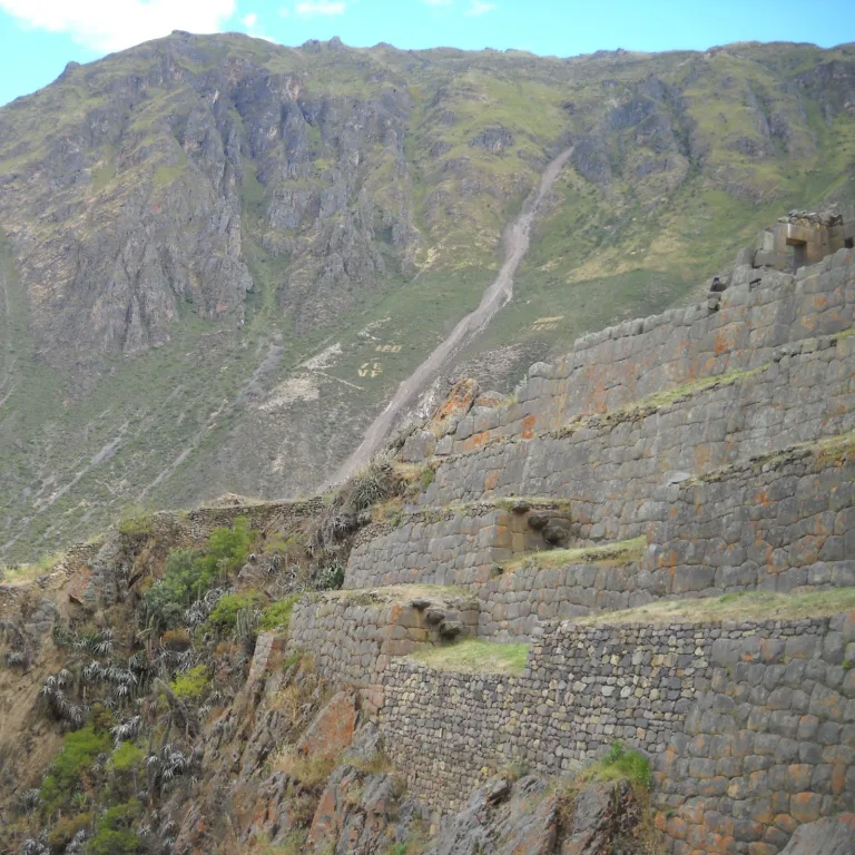 Angled view of Inca terraces on Temple Hill at Ollantaytambo with mountain backdrop and stone construction detail.