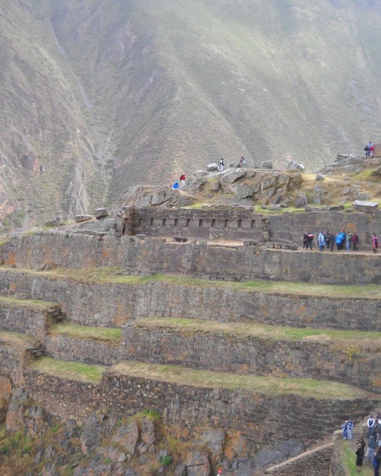 Inca terraces and the Temple of the Sun at Ollantaytambo, with visitors exploring the stone structures against a backdrop of steep Andean mountains in the Sacred Valley of Peru