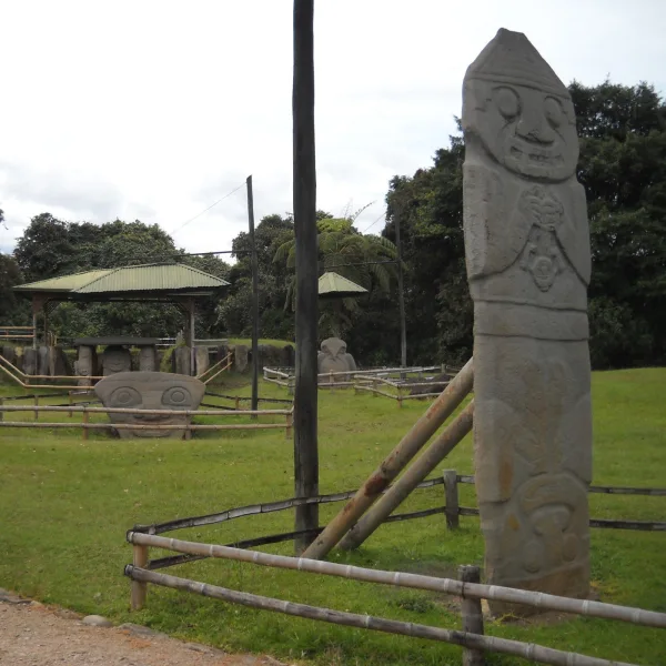 Overview of San Agustín Archaeological Park with standing statues and carved monoliths surrounded by railings and grassy landscape