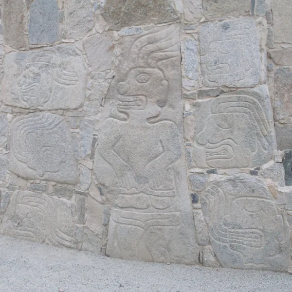 Full-body stone carving of a warrior flanked by dismembered heads and limbs on the wall at Cerro Sechín.