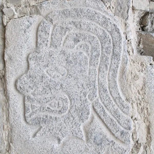 Stone relief from Cerro Sechín depicting a warrior's head in profile with stylized hair and angular jaw.