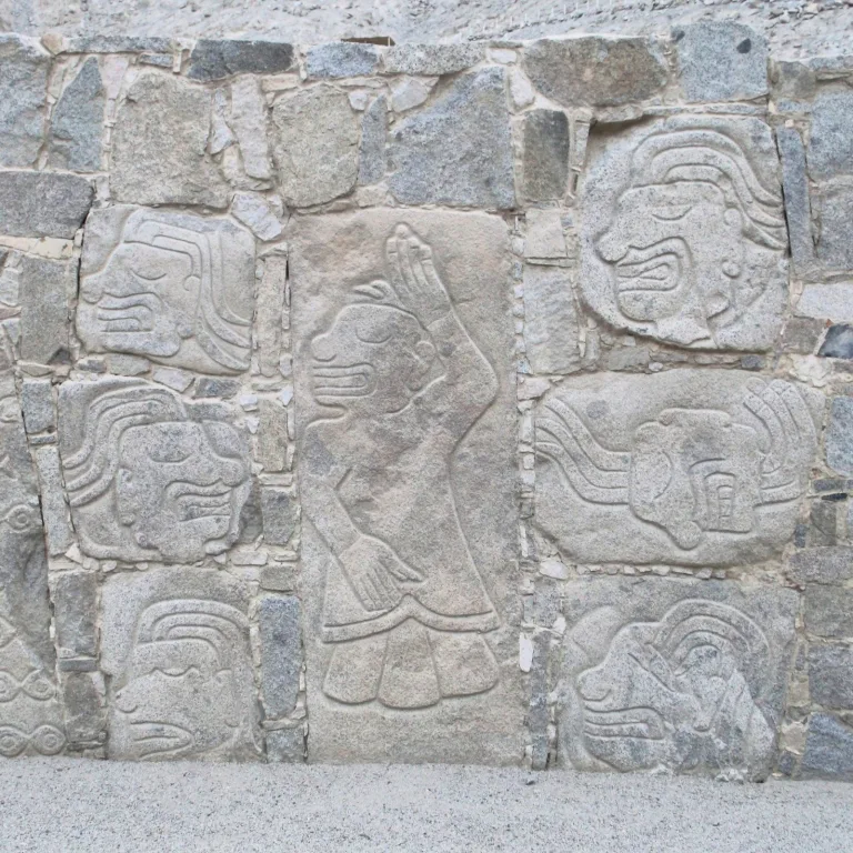 Close-up of engraved stone wall at Cerro Sechín showing dismembered figures and warrior-priest faces from the Casma–Sechín culture