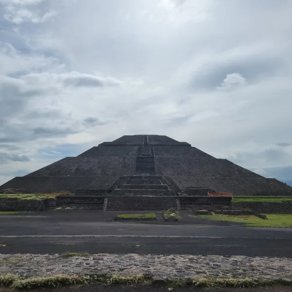 Front view of the Pyramid of the Sun at Teotihuacan under a dramatic sky, showing its central staircase and terraced design.