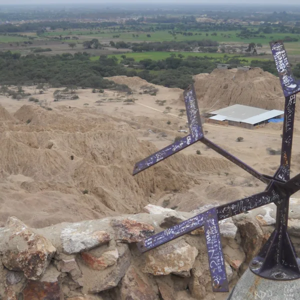 Overhead view of the Túcume pyramids from Cerro Purgatorio, with green valley in the distance and a metal directional marker in the foreground