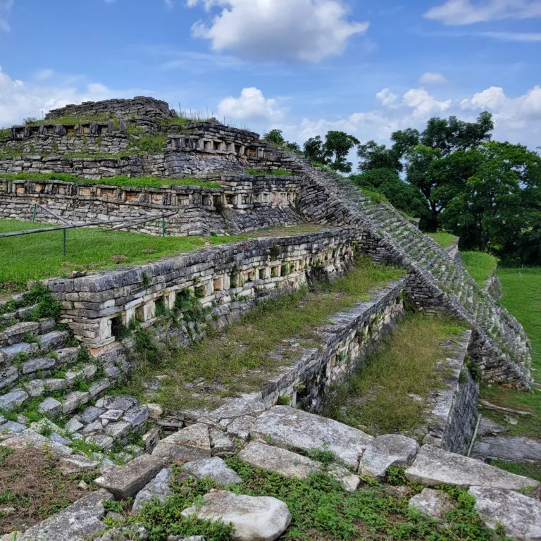 A low, rectangular stone platform at Yohualichan featuring a central staircase flanked by steps, set against a tree-lined ridge.