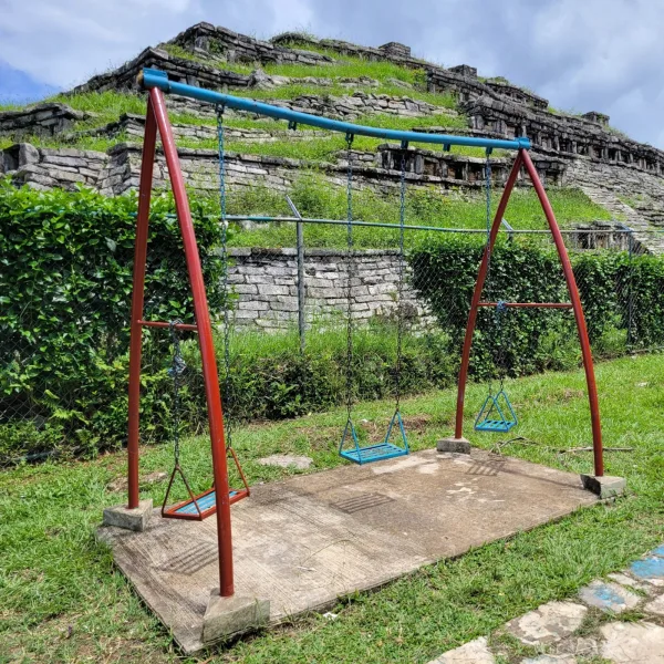 Temple mound at Yohualichan seen behind a modern swingset and manicured grass—contrast of ancient and contemporary elements.