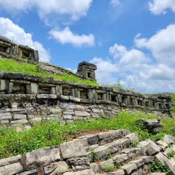 Flat-topped ruin platform with niches and stacked stone construction and steps, framed by dense greenery at Yohualichan.