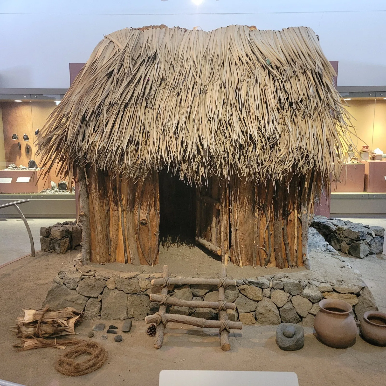 Reconstruction of a traditional Cantona dwelling with thatched roof, stone base, and obsidian tools on display in a museum exhibit