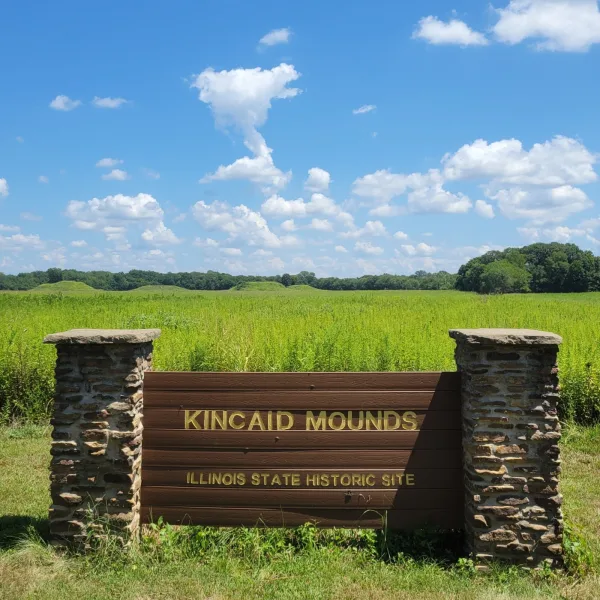 Wooden sign marking the entrance to Kincaid Mounds in southern Illinois, with the ancient earthworks visible across the fields.