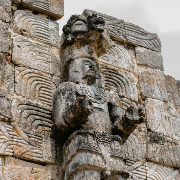 Detailed stone carving of a standing warrior or ruler with ornate headdress and jewelry at Uxmal