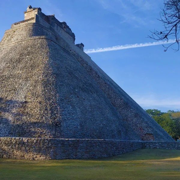 Massive sloped face of the Pyramid of the Magician rising steeply under blue skies at Uxmal