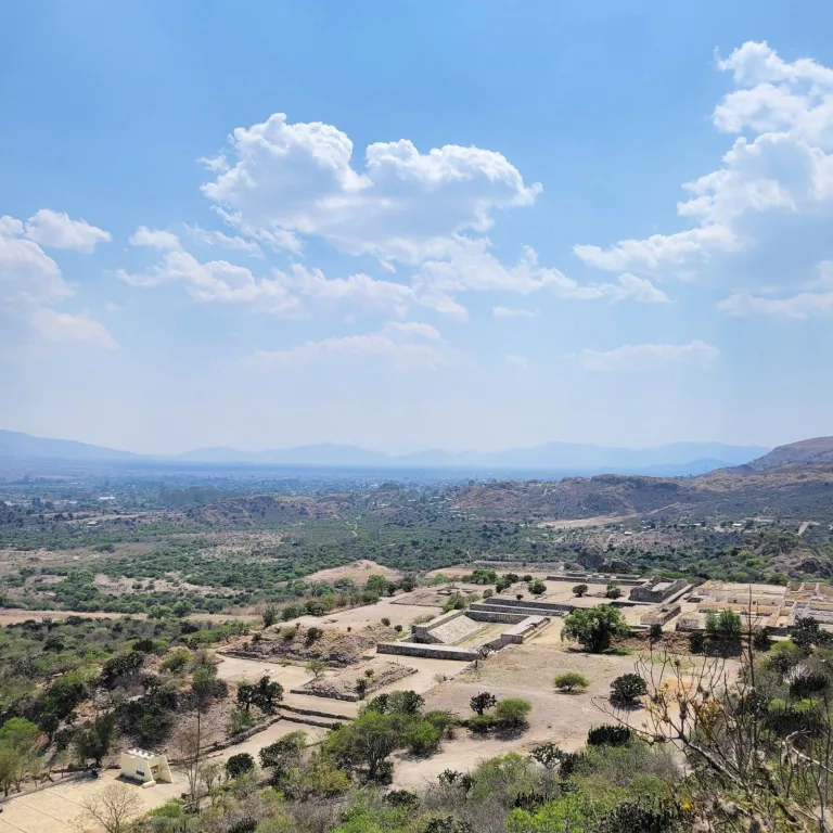 Panoramic view from the fortress ruins of Yagul in Oaxaca, Mexico, showing the ballcourt, terraced platforms, and surrounding valley landscape.