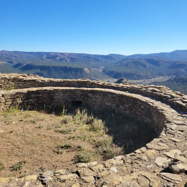 Closeup view of the interior curved stone wall of a Kiva, with a small rectangular tunnel entrance visible in the masonry.