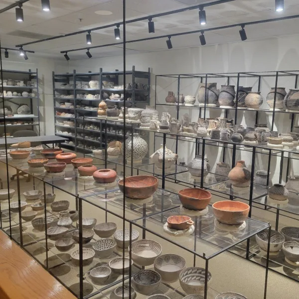 Interior view of a museum exhibit area featuring a large window that looks into the visible archaeology lab and workspace.