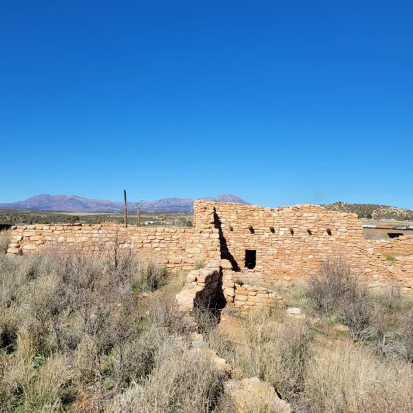 Ground-level view of the preserved main Ancestral Puebloan masonry structure, showing its standing square and rectangular walls in the arid landscape.