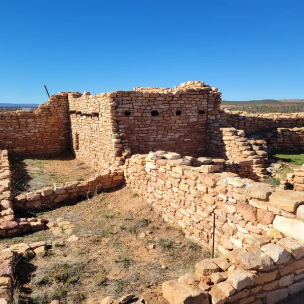Exterior view of the preserved Ancestral Puebloan masonry structure at the site, showing low standing walls and the arid landscape surrounding the ruin.