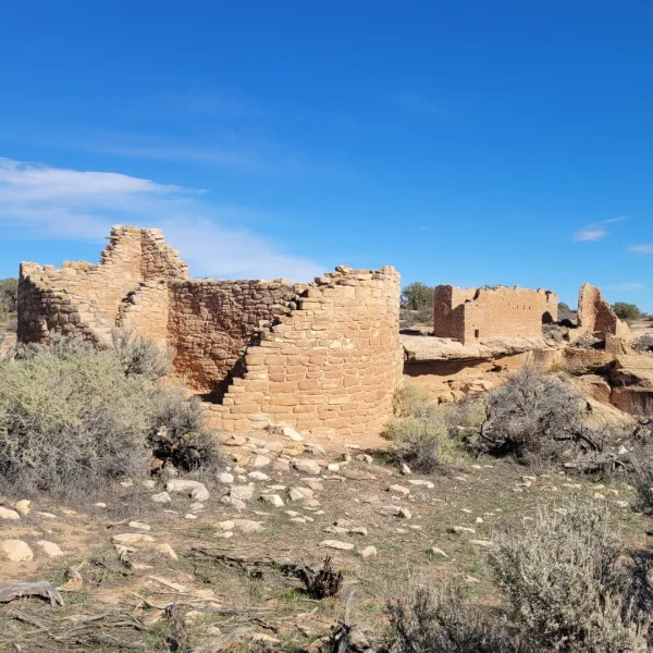 Ruins of an Ancestral Puebloan structure in the foreground with the famous Hovenweep Castle visible across the deep canyon in the background.