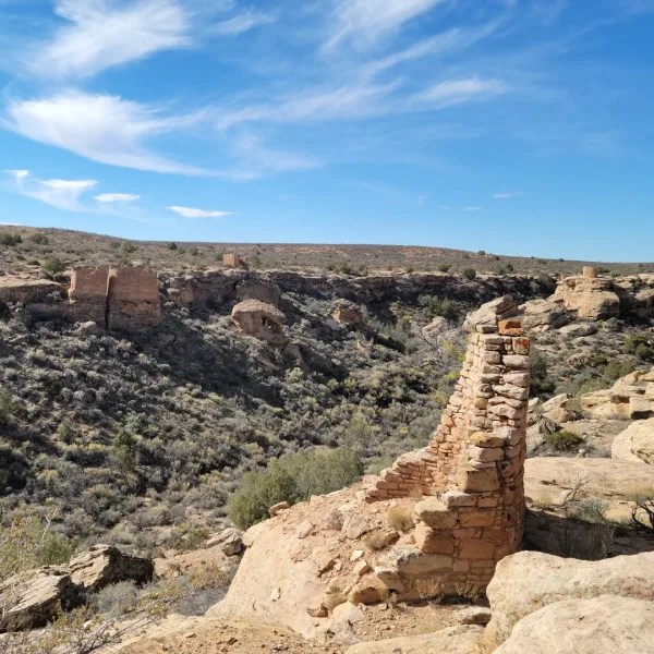Long-distance view of the ruins known as Hovenweep Stronghold House, built on a narrow neck of rock overlooking a deep, wide canyon.