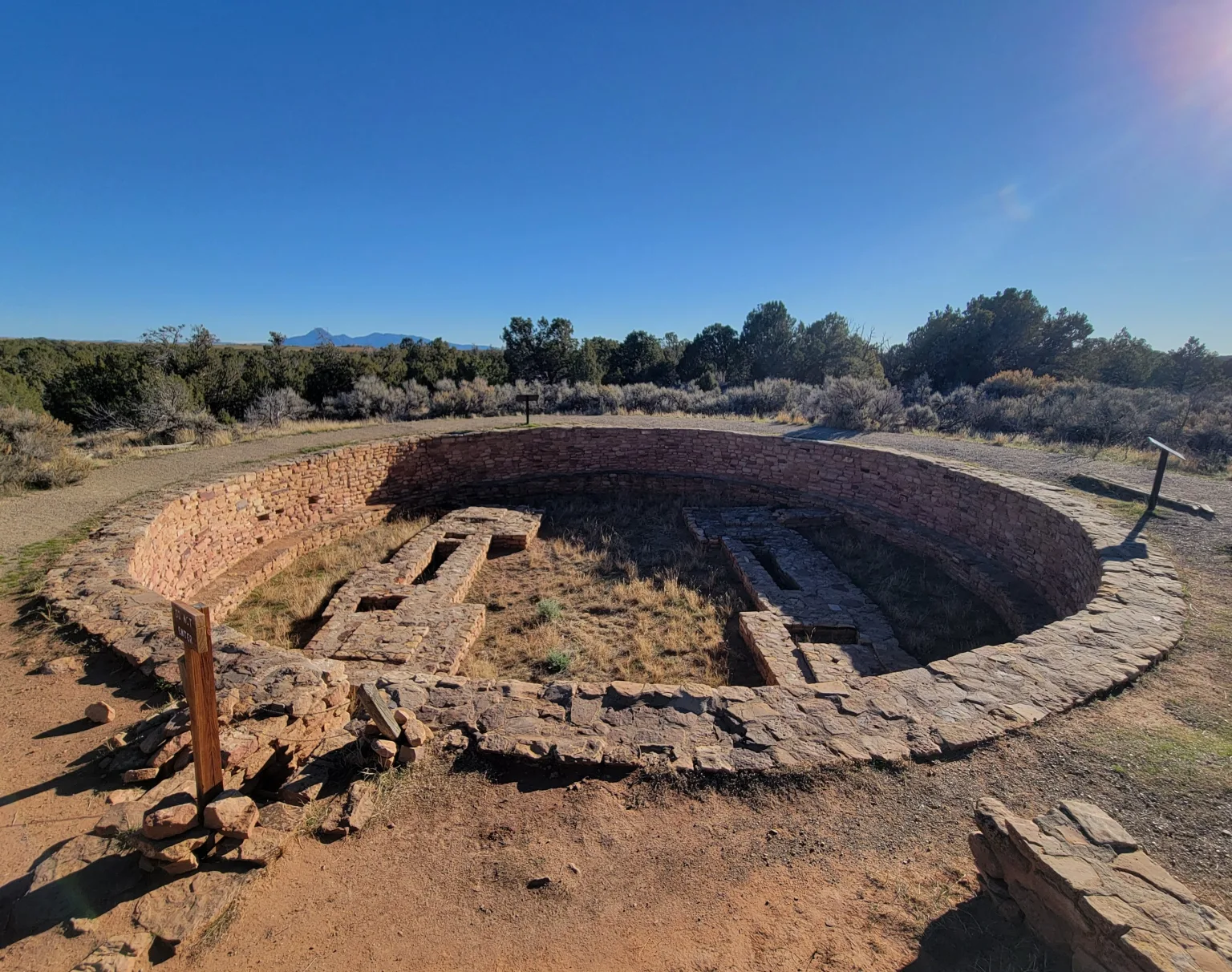 Downward view into the large, circular, subterranean Great Kiva at Lowry Pueblo, showing the massive depth and the small circular stone features (pedestals/figures) on the kiva floor.