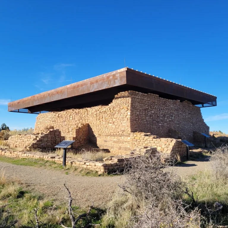View of the central Lowry Pueblo ruins, showing the excavated T-shaped room block and kivas protected by a large, modern, flat reconstructed shelter.
