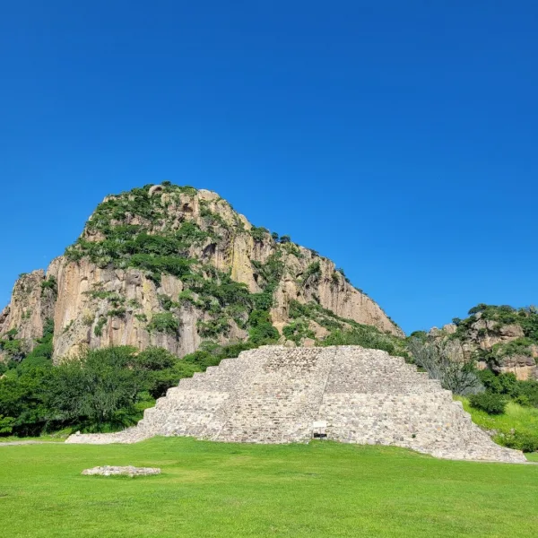 Stone platform pyramid at Chalcatzingo set in a grassy plaza with the steep rocky face of Cerro Chalcatzingo rising directly behind the structure.