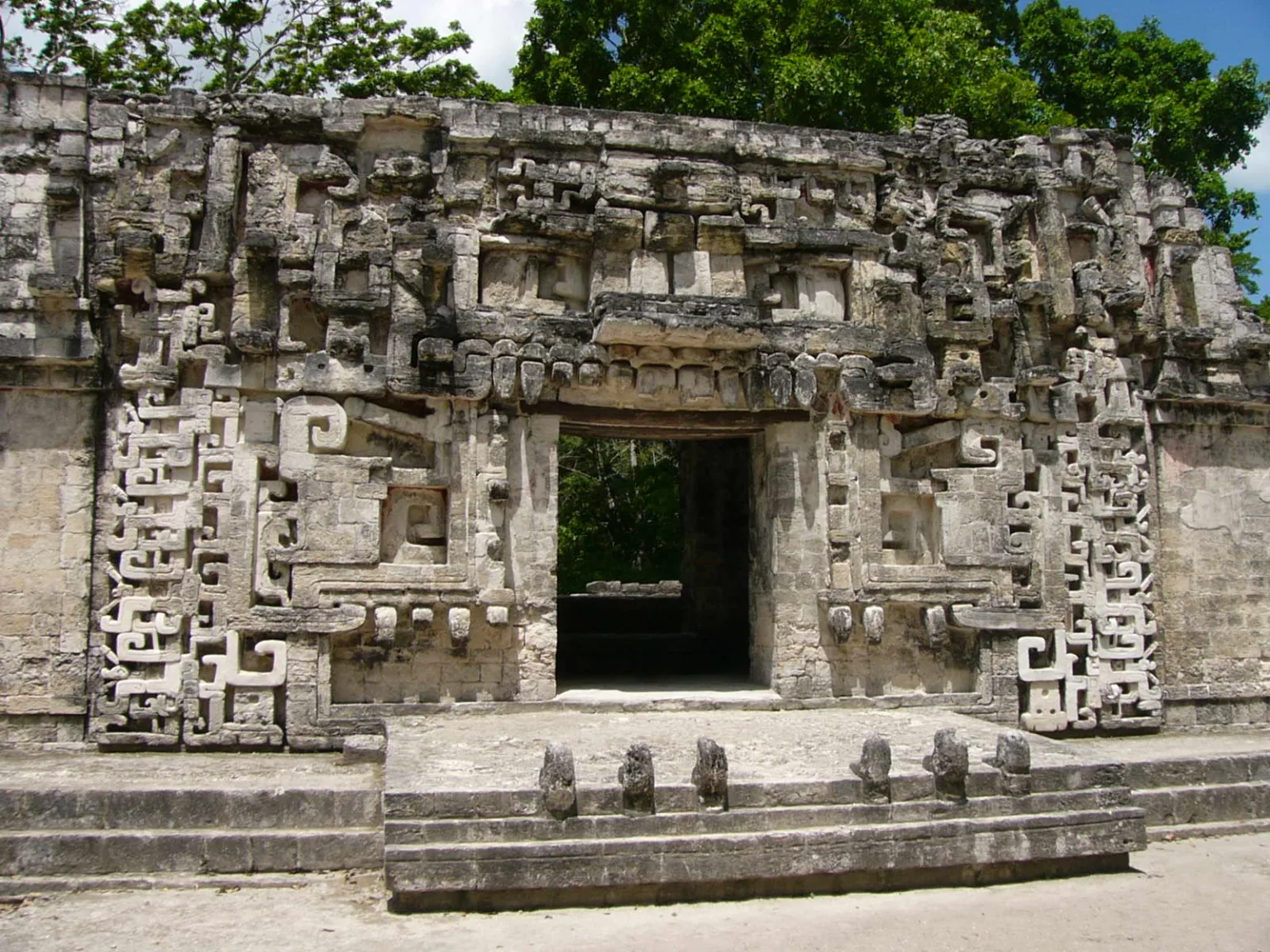 Stone façade of Structure II at Chicanná, a Maya site in Campeche, Mexico, showing an ornate Rio Bec style gateway carved as a stylized monster mouth with geometric stone mosaics.