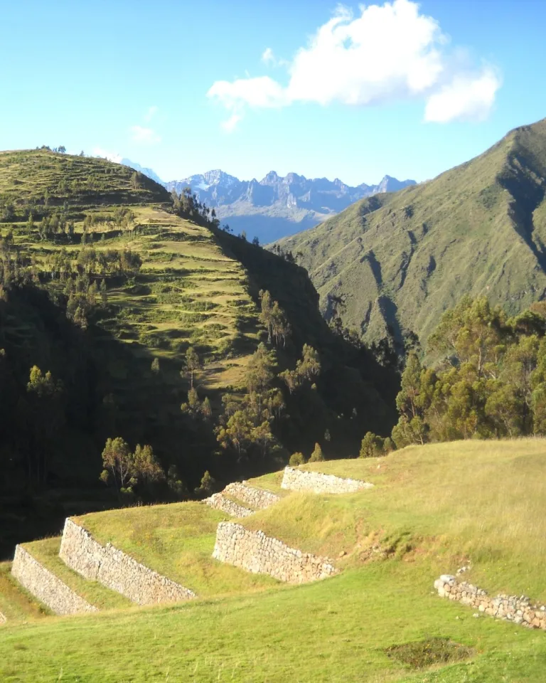 Stone agricultural terraces at Chinchero set along a grassy hillside in the Andean highlands with mountains rising in the distance.
