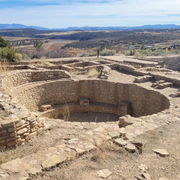 Reconstructed Great Kiva at Escalante Pueblo in Dolores, Colorado showing the circular stone chamber with interior bench and surrounding room blocks overlooking the Dolores River valley.