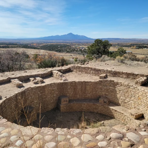 Reconstructed Great Kiva at Escalante Pueblo in Dolores, Colorado with circular stone chamber and interior bench overlooking the Dolores River valley and Ute Mountain in the distance.