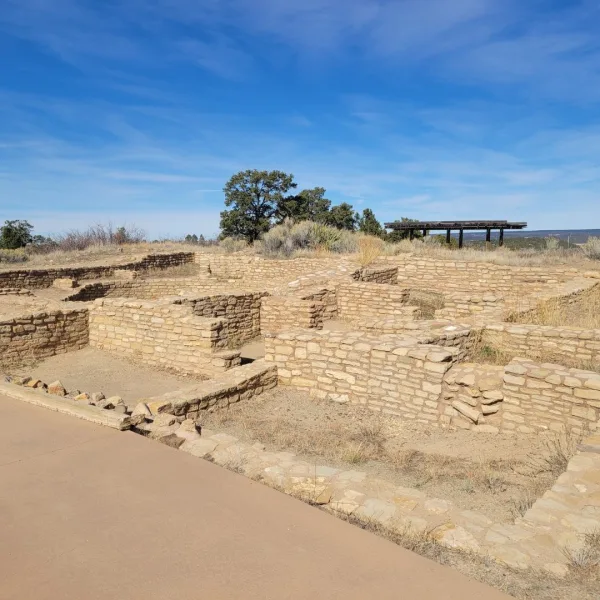 Reconstructed masonry room blocks at Escalante Pueblo in Dolores, Colorado with interpretive walkway and shelter structure visible in the background.