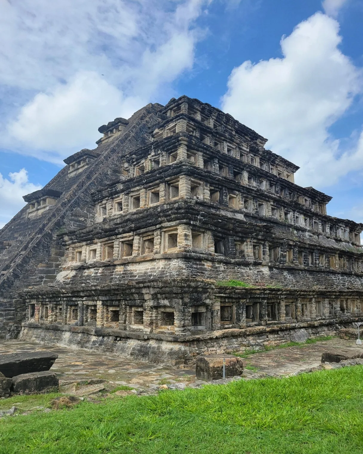 Pyramid of the Niches at El Tajin in Veracruz Mexico with stepped tiers and rows of square niches beneath a blue sky.