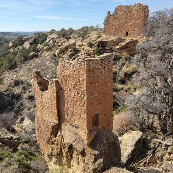 Holly Tower at the Holly Group in Hovenweep National Monument, a multi-story Ancestral Puebloan tower built atop a large sandstone boulder, with Holly House on the canyon rim behind it.