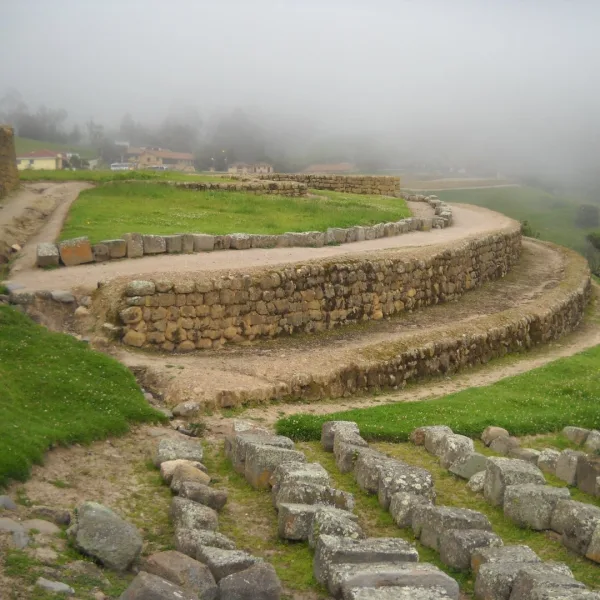 Curved stone terraces at Ingapirca in Canar Ecuador seen in fog with grassy platforms and a winding path.