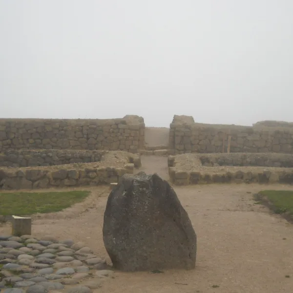 Standing stone among low stone foundations at Ingapirca in Canar Ecuador seen in fog.
