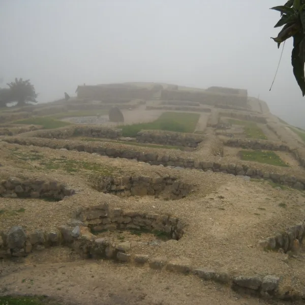 Foggy view of low stone foundations at Ingapirca in Cañar, Ecuador, with the Temple of the Sun area in the background.