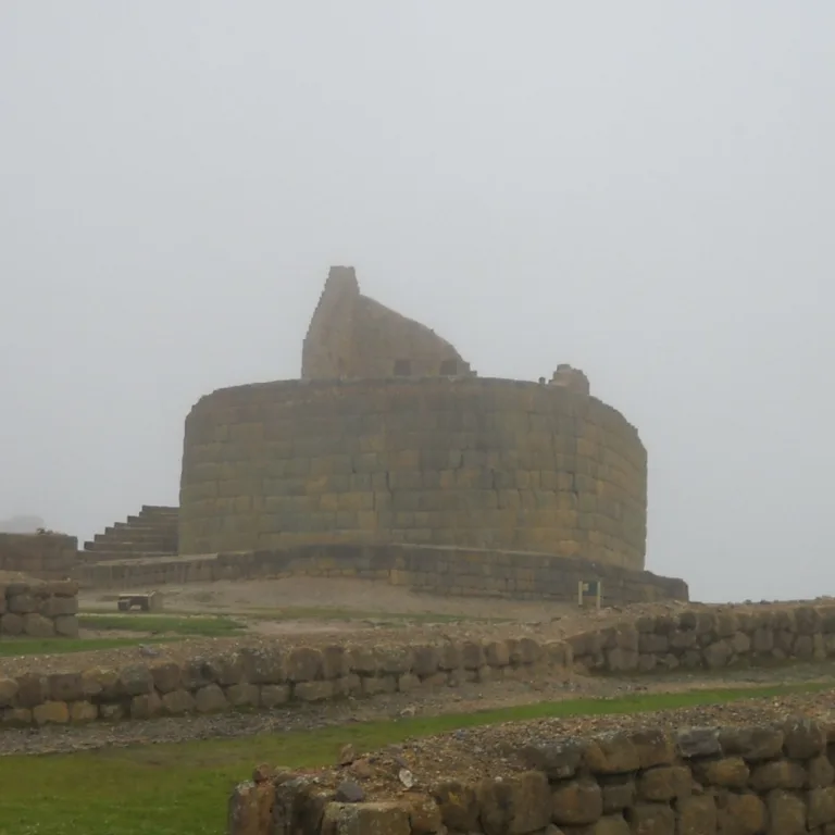 Temple of the Sun at Ingapirca in Cañar, Ecuador, seen through fog with low stone walls in the foreground.