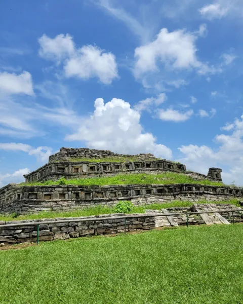 Pyramid with niches at Yohualichan near Cuetzalan Mexico with stepped stone terraces rising above a grassy foreground.
