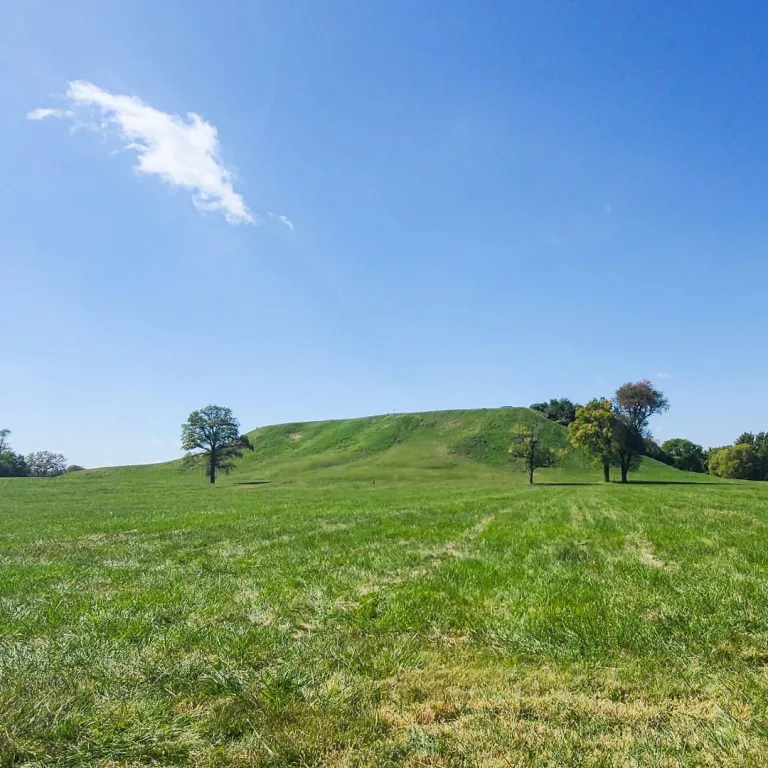 Monks Mound at Cahokia Mounds in Illinois, with a large grass-covered Mississippian platform mound rising above an open field.