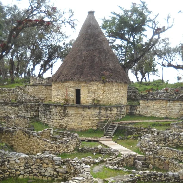 Circular stone house at Kuélap in Chachapoyas, Peru, with a reconstructed thatched roof above surrounding ruins.