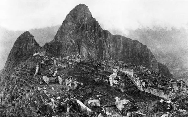 Black and white 1912 photograph of Machu Picchu after clearing work, showing Inca terraces, stairways, stone ruins, and Huayna Picchu behind the site.