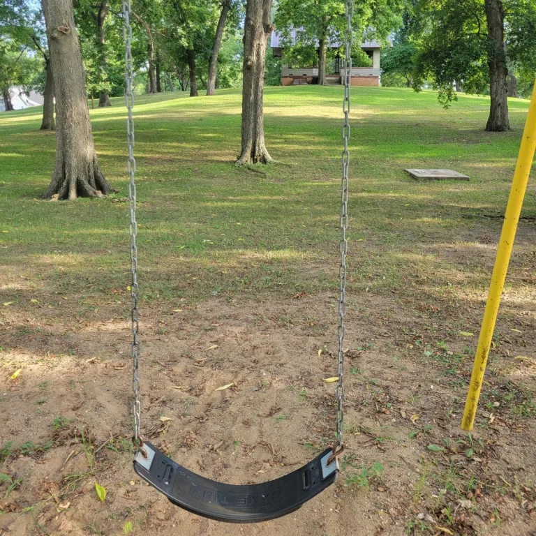 View from the playground swing area toward Rockwell Mound in Havana, Illinois, with the grassy mound slope, trees, and shelter at the top.