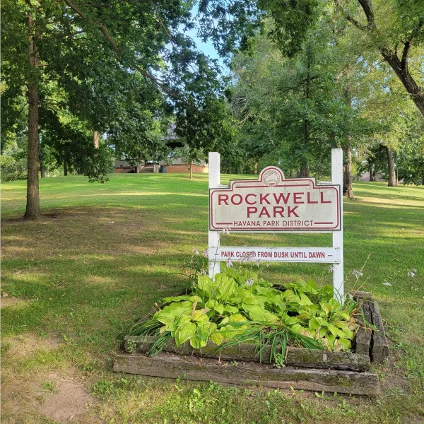 Rockwell Park sign in Havana, Illinois, with the grassy slope of Rockwell Mound and the mound-top shelter visible behind the entrance sign.